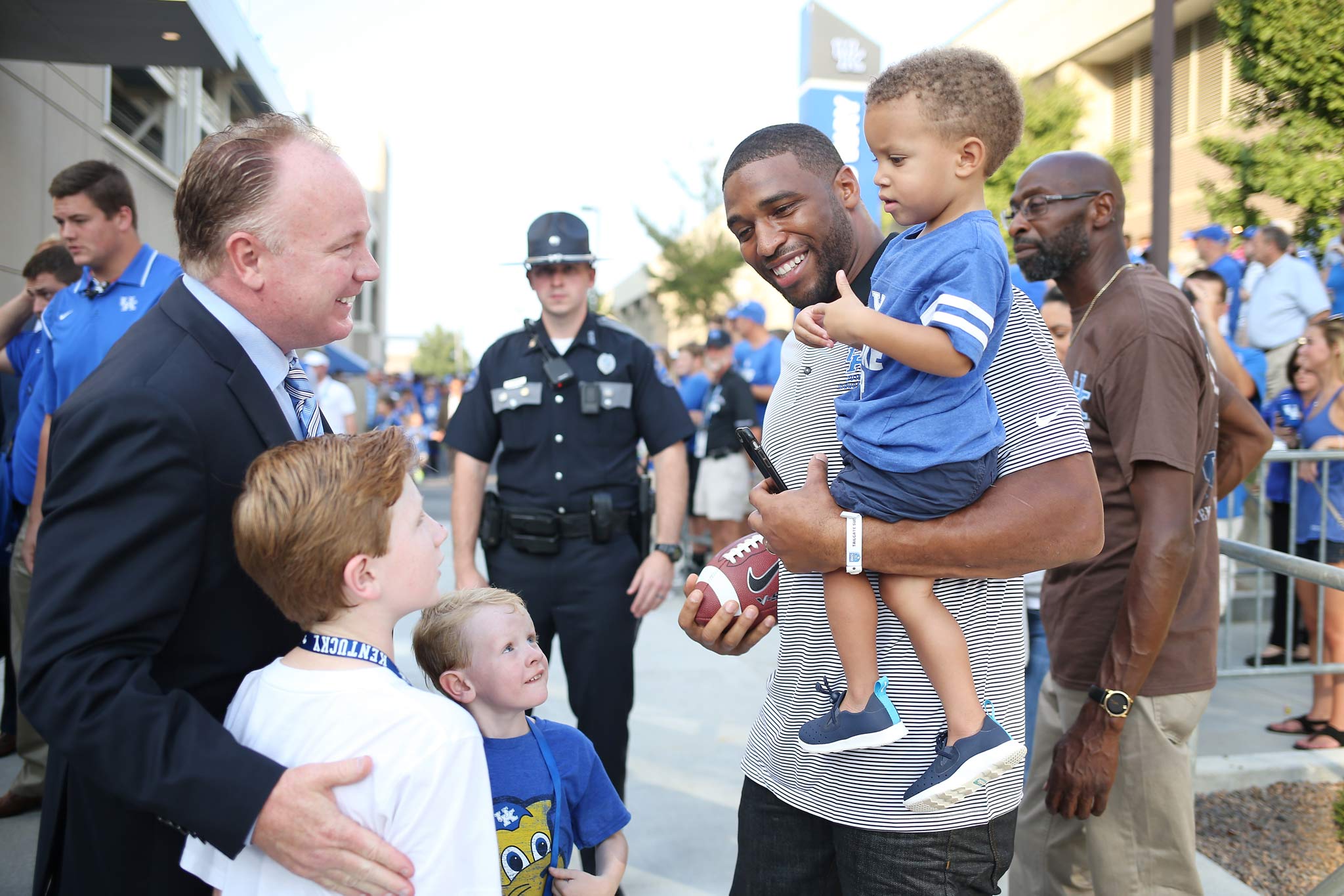 Coach Stoops and his two sons talk with Wesley Woodyard, a former UK linebacker, who is carrying a little boy in his arms.