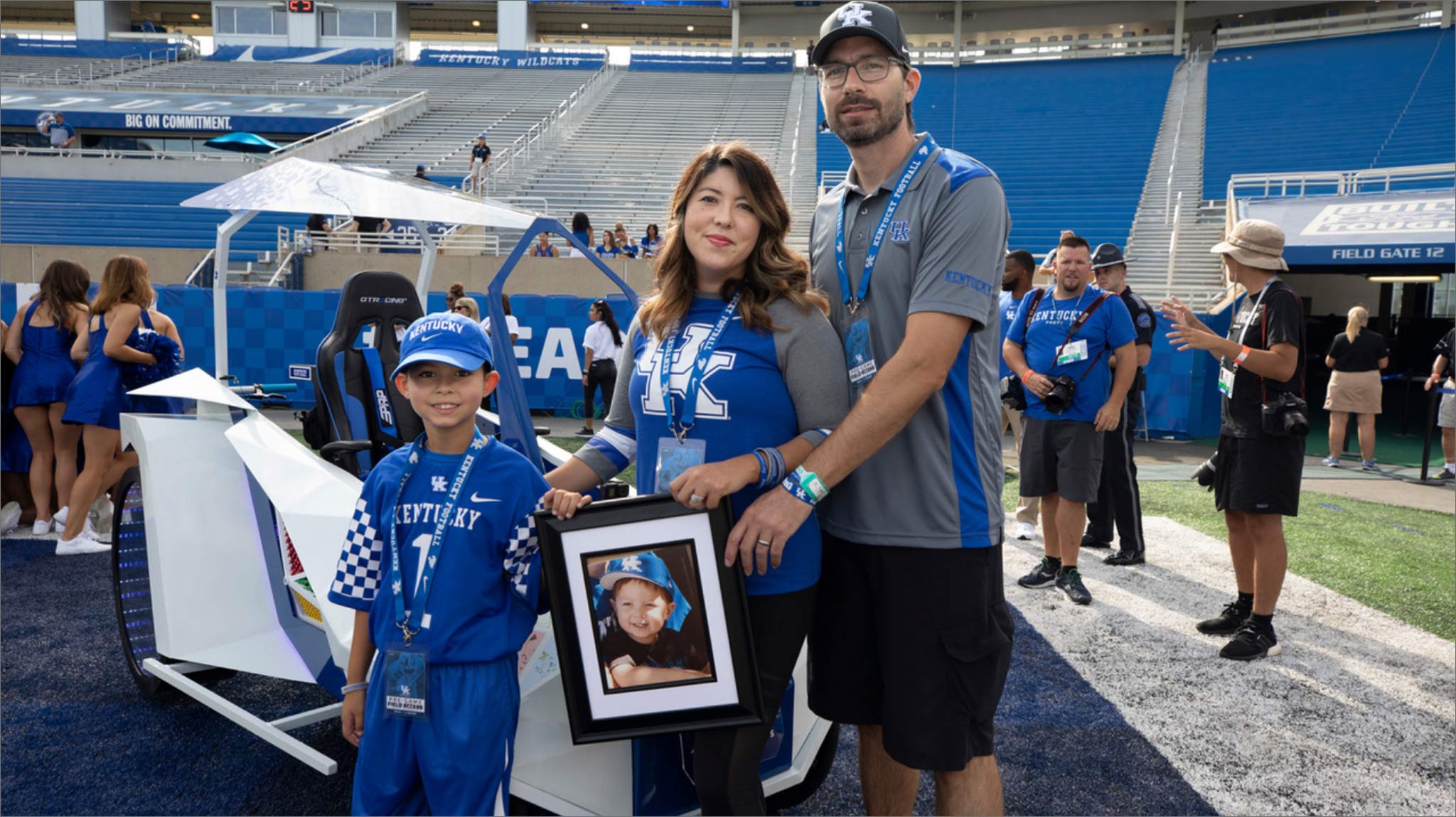 Liz, Benjamin, and Maximo prepare to lead the UK Football season opener, the Cat Walk. Liz holds a framed portrait of Marco.