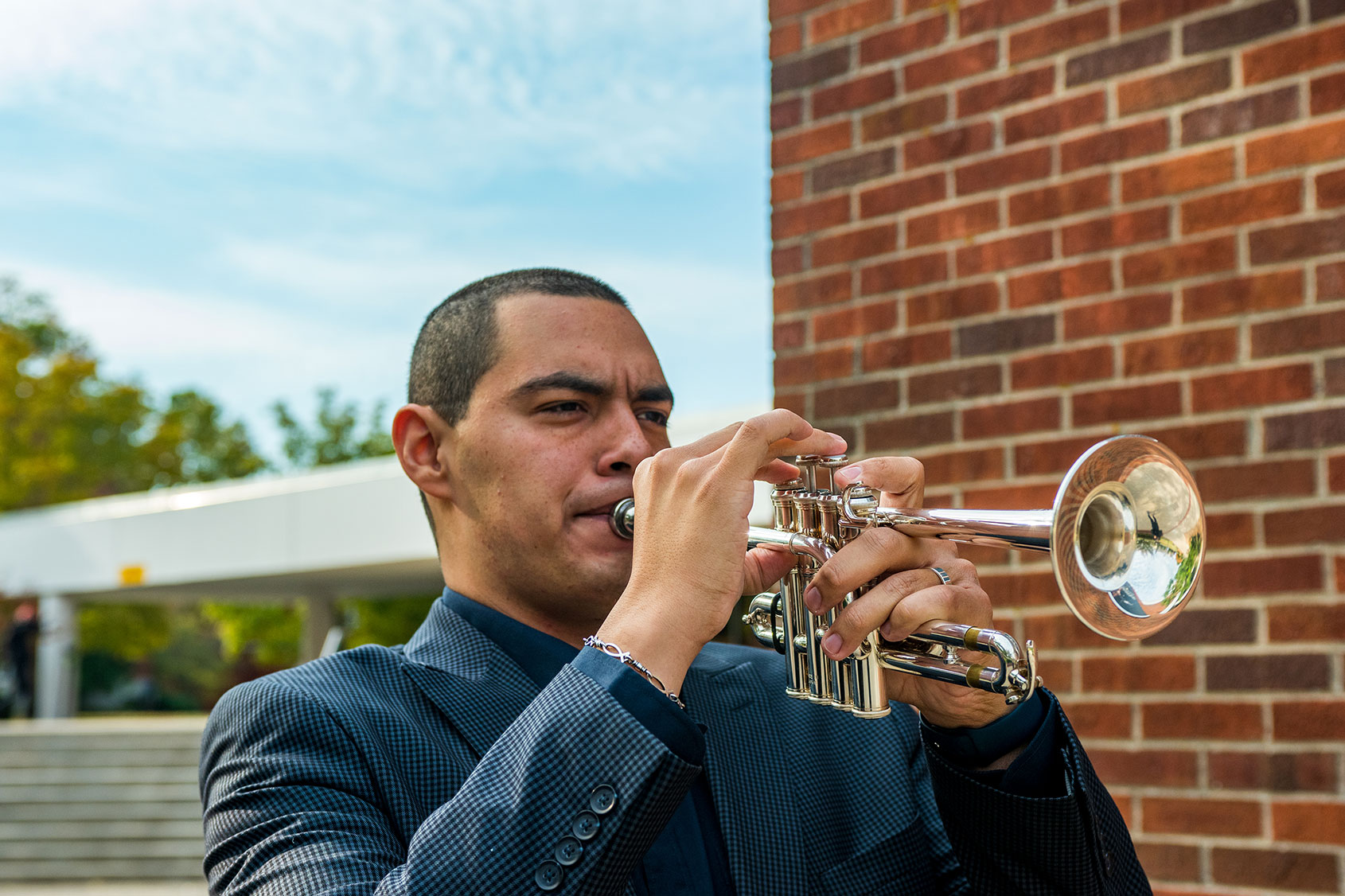 Adiel Nájera plays his trumpet while standing outside on the University of Kentucky campus.