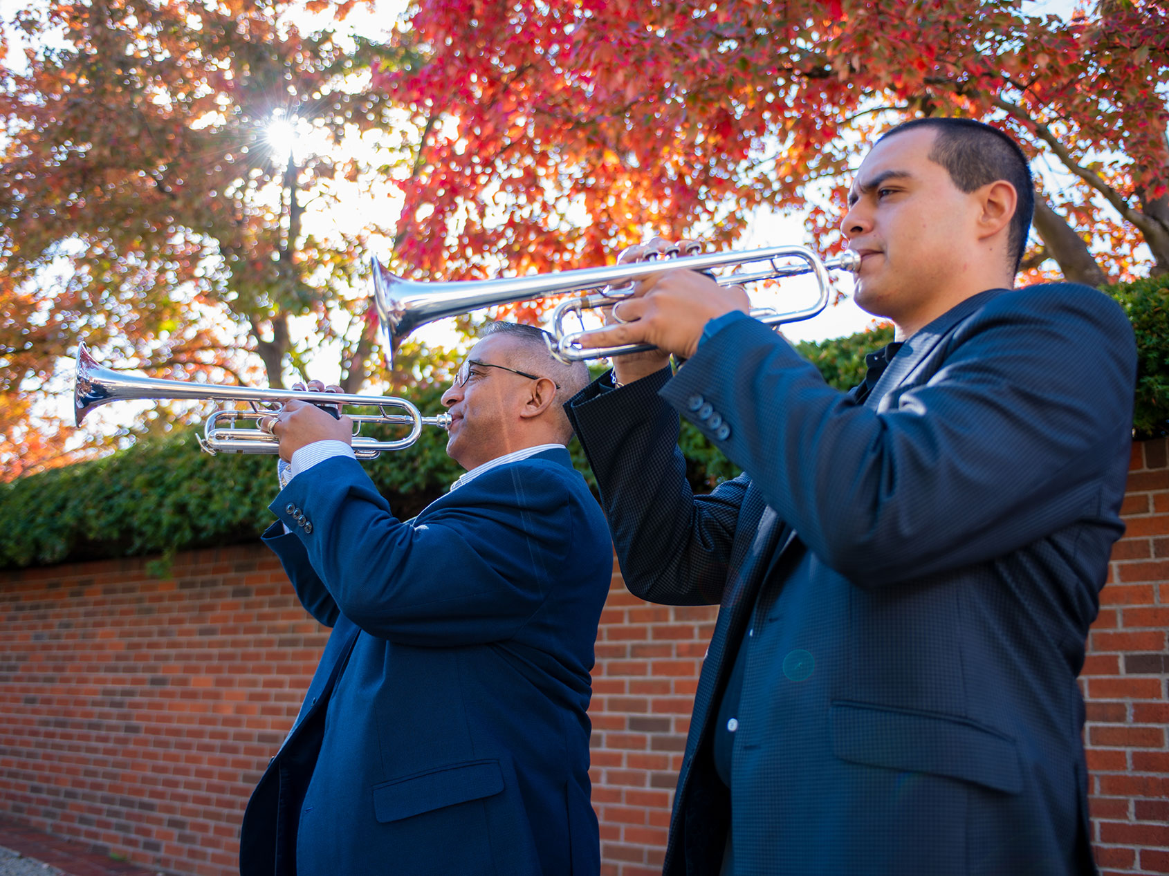 Adiel Nájera and his father play their trumpets together while standing outdoors on the University of Kentucky campus.