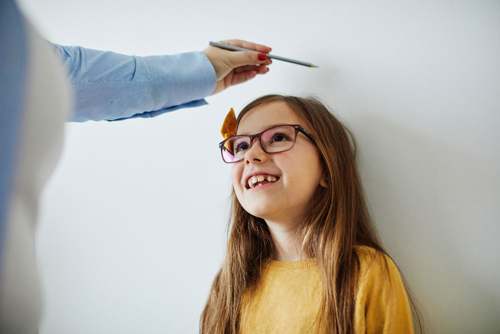 A parent marks the height of their daughter on a wall by using a pencil.