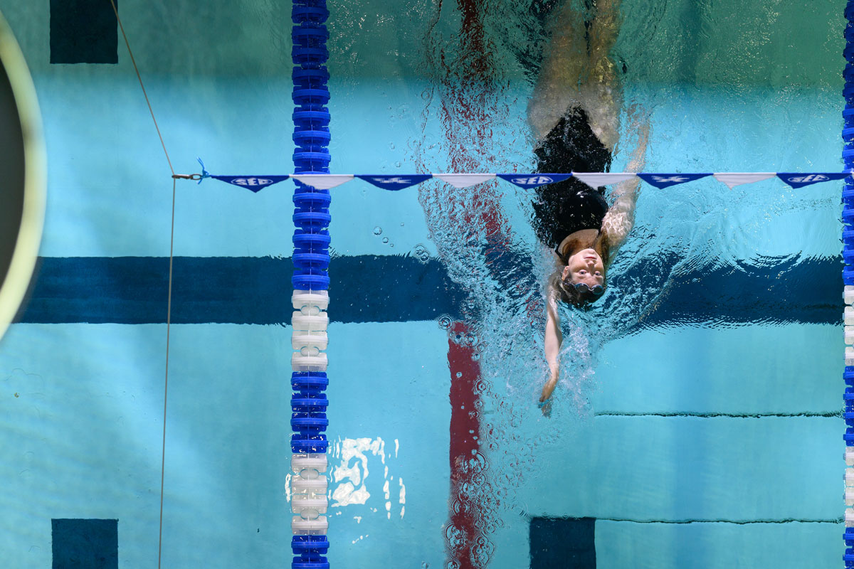 Alayna Benningfield performing a backstroke in a swimming pool, shot from overhead.
