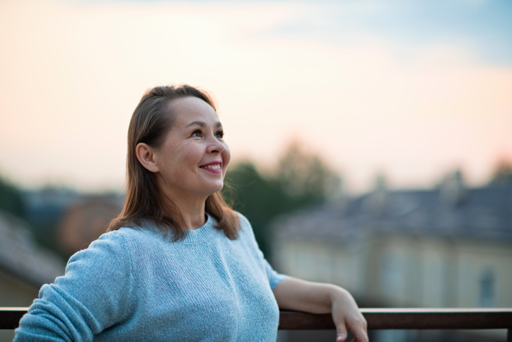 A woman, framed to the left, looks to the right with a soft smile on her face as the sun appears to rise.