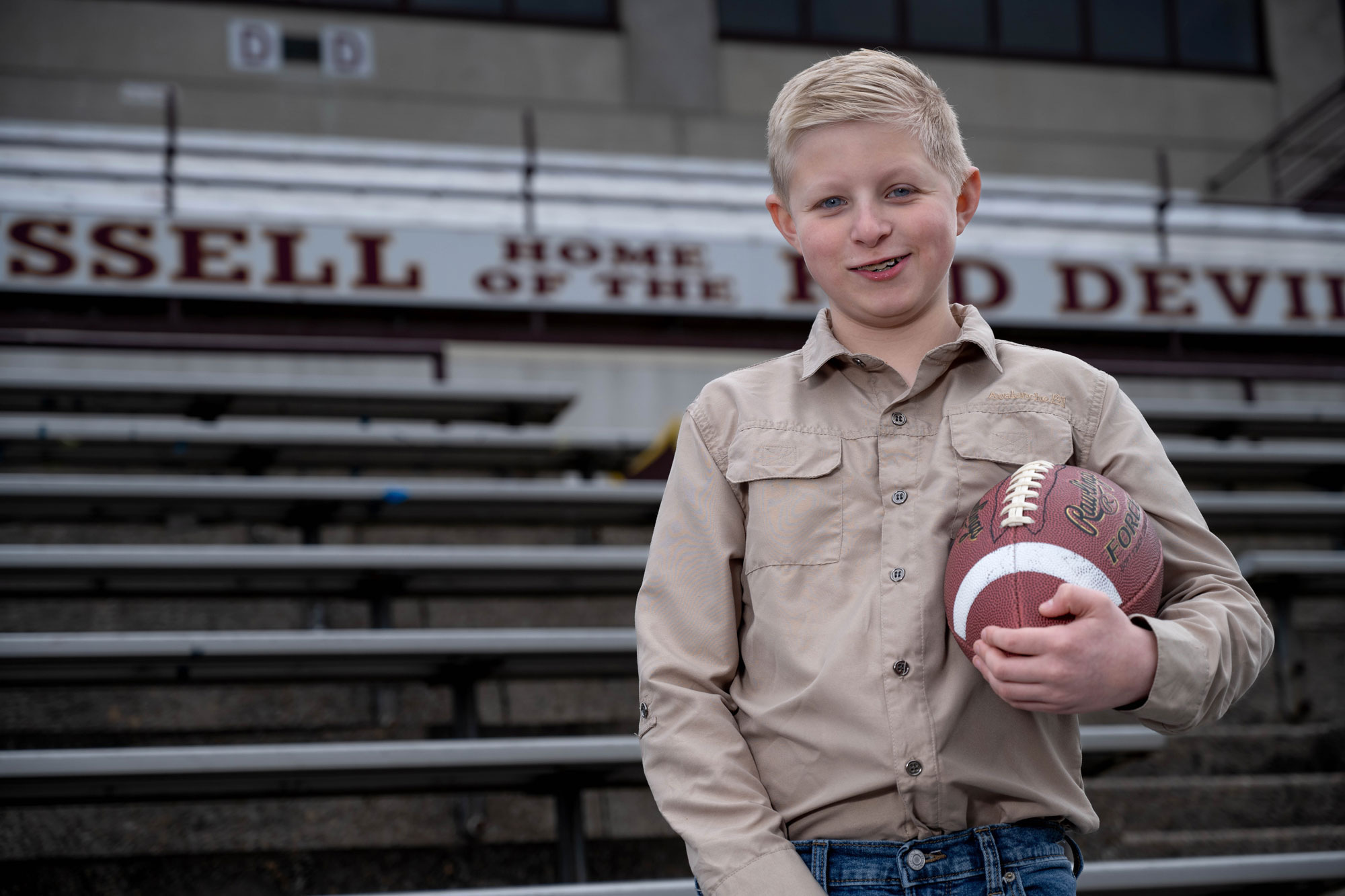 William Dean holding a football in the stands of the Russell High School football stadium