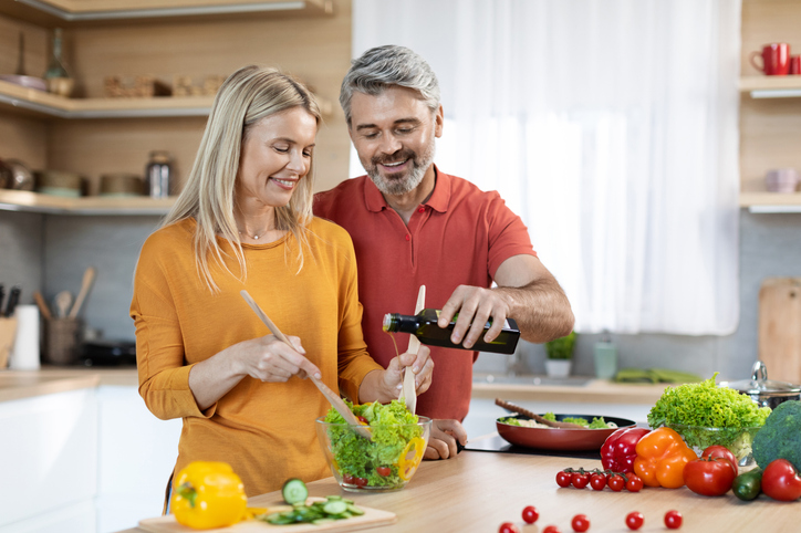 A man and a woman, likely a couple, prepare a salad together