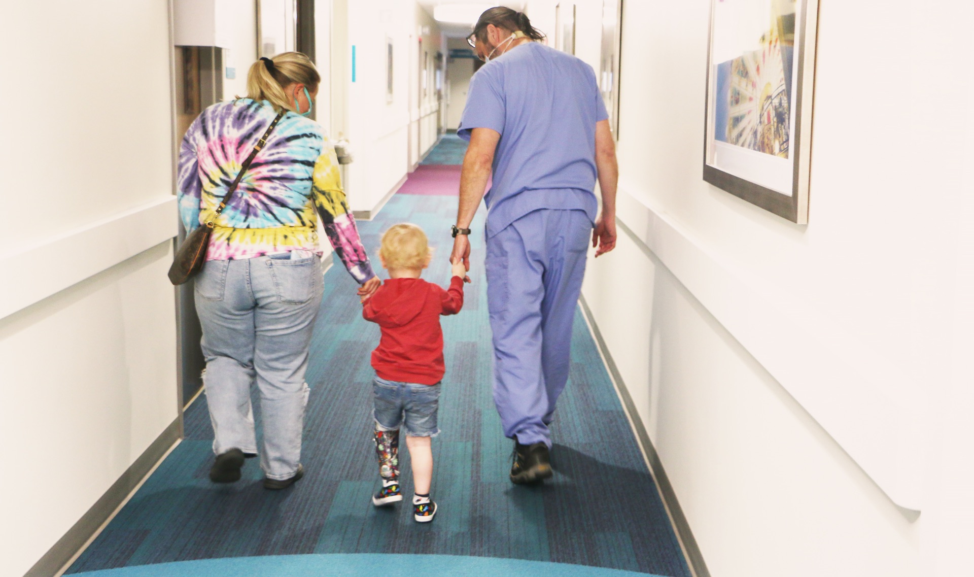 Arlo Yost is walking between his mother and Dr. Talwalkar, holding their hands as they make their way down the hallway.