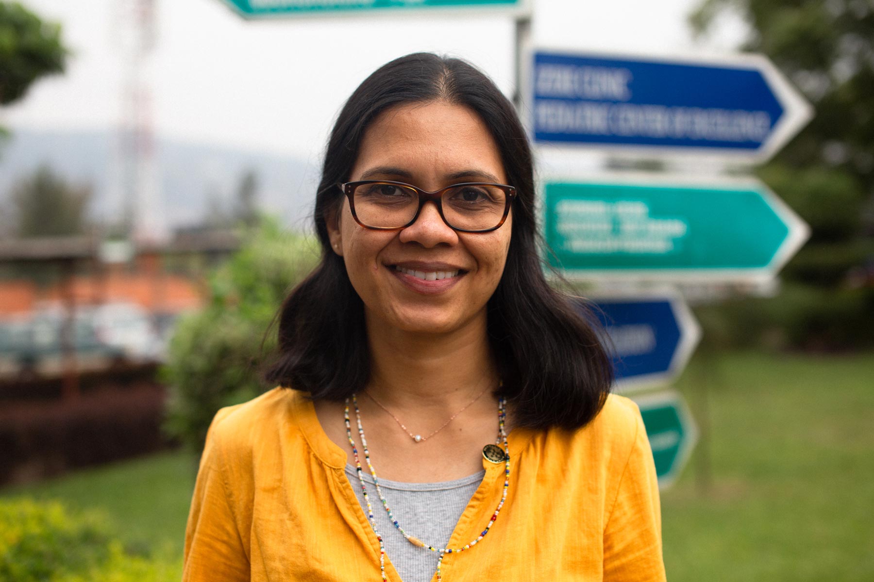 Dr. Shenoi smiles in front of a signpost outside.