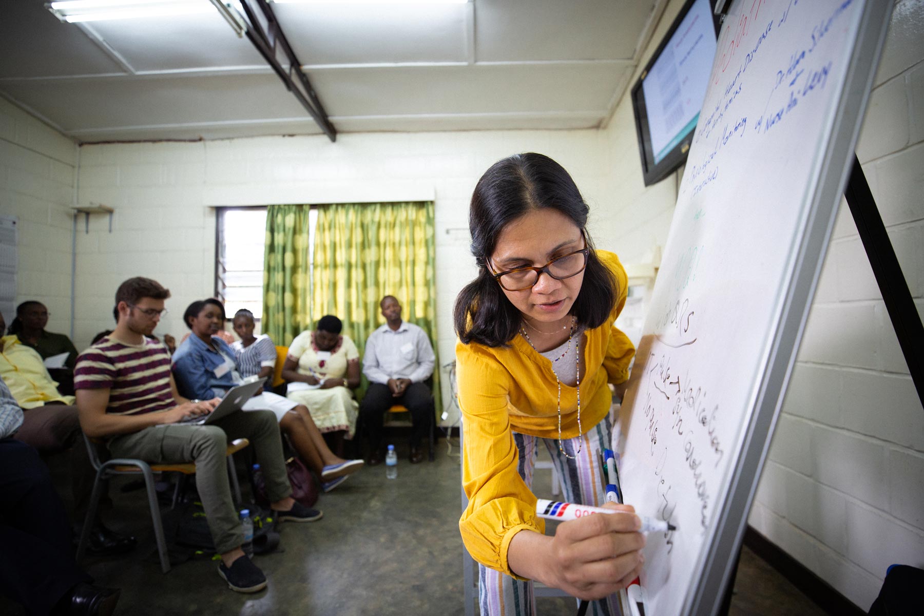 Dr. Shenoi writes on a whiteboard while training with doctors and nurses in Rwanda.