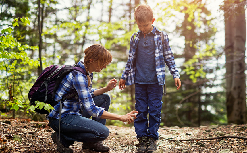 A mother applies insect repellant to her son's clothing.