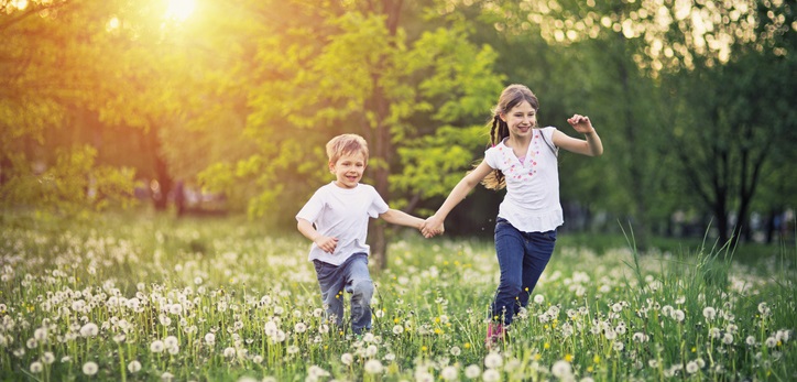 Brother and sister run together in a field.