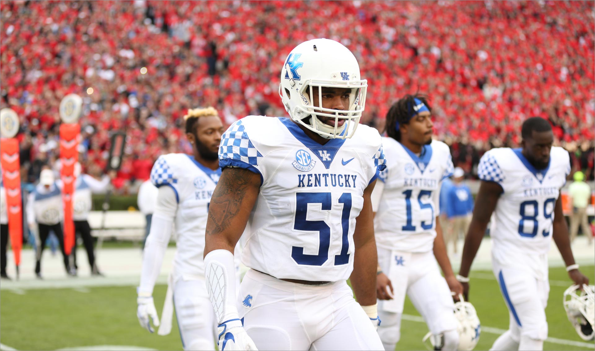 In another photo from his college football days, Courtney walks onto the field with his team. He is wearing a helmet and a white Kentucky jersey with #51 on it.