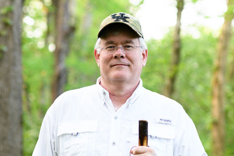 Dr. McLarney hikes with a walking stick in a forest.