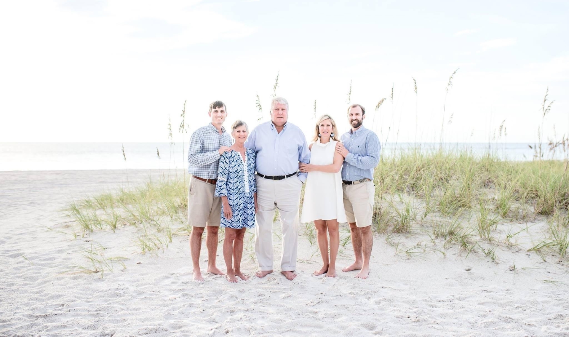 E and her family pose for a group photo on a sandy dune with long grass at the beach.