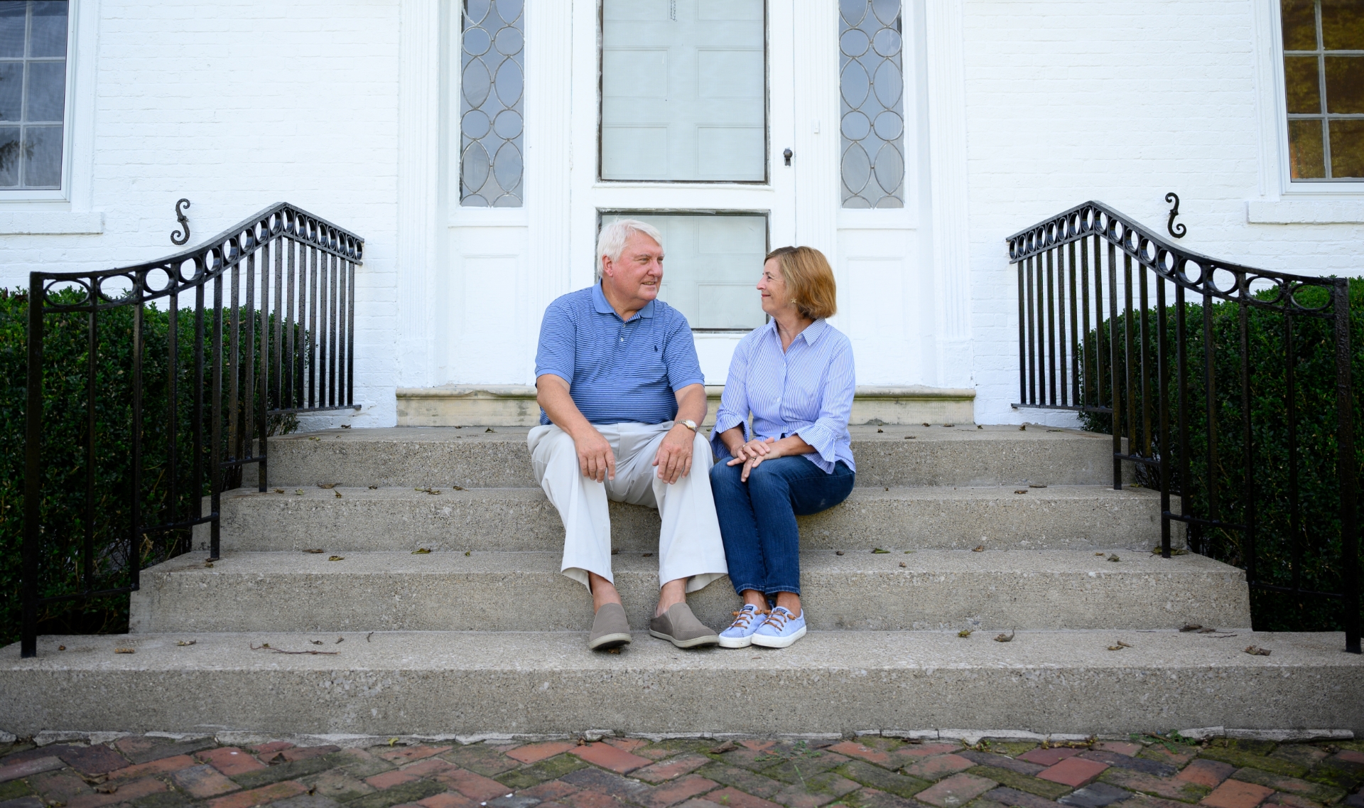 E and Cary sit on the front steps of their home, looking at each other and smiling.