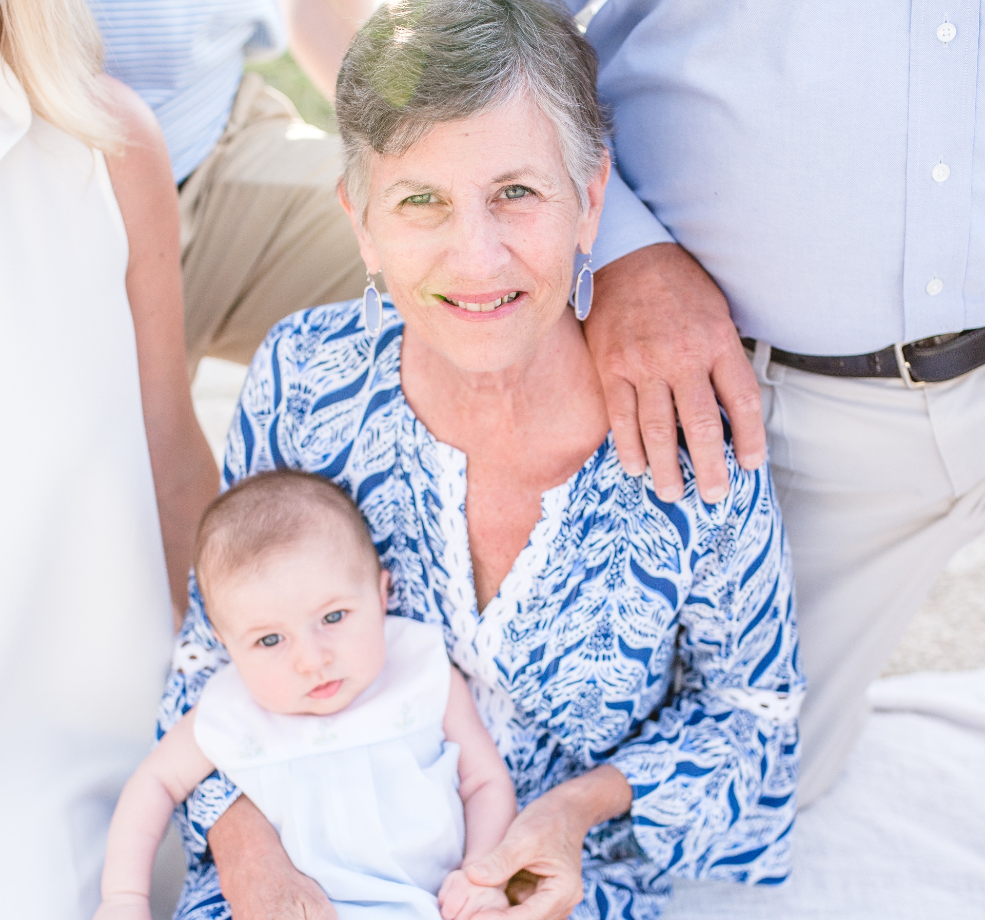An older photo of E, with short grey hair, holding her grandchild and surrounded by family members.