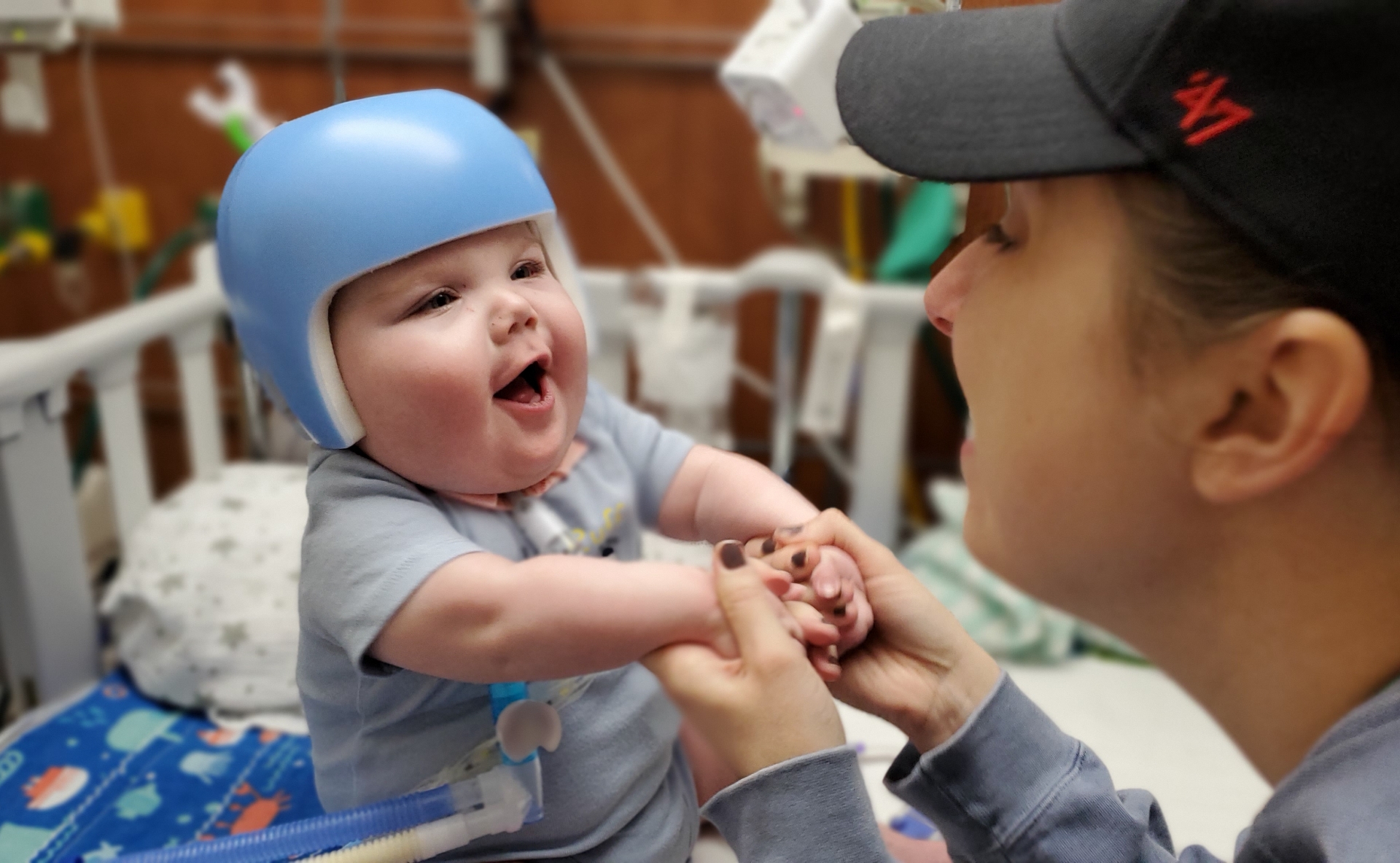 A candid photo of Claire gently playing with baby Everett, who is wearing a cranial helmet.