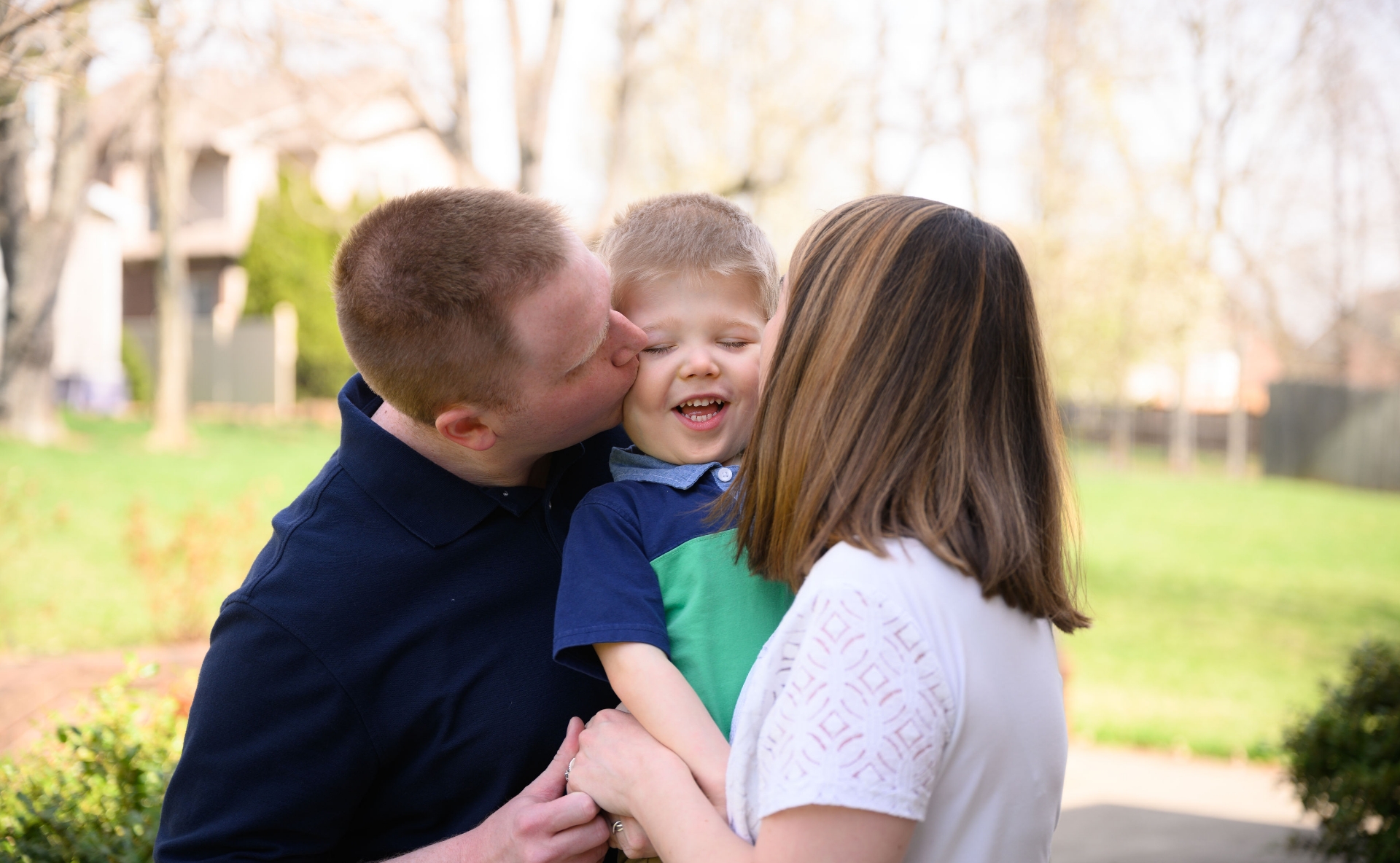 A photo of Claire and Daniel holding Everett while they each kiss Everett’s cheek.