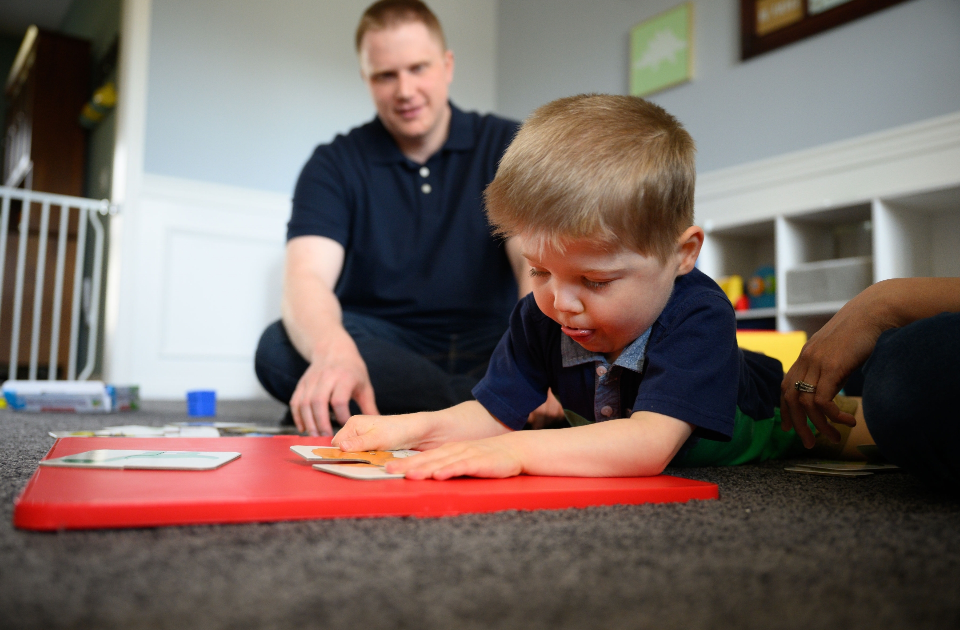A close-up of Everett playing with his toys on the floor as Daniel watches on.