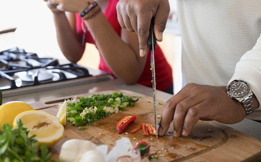 A father chops vegetables while his children watch.