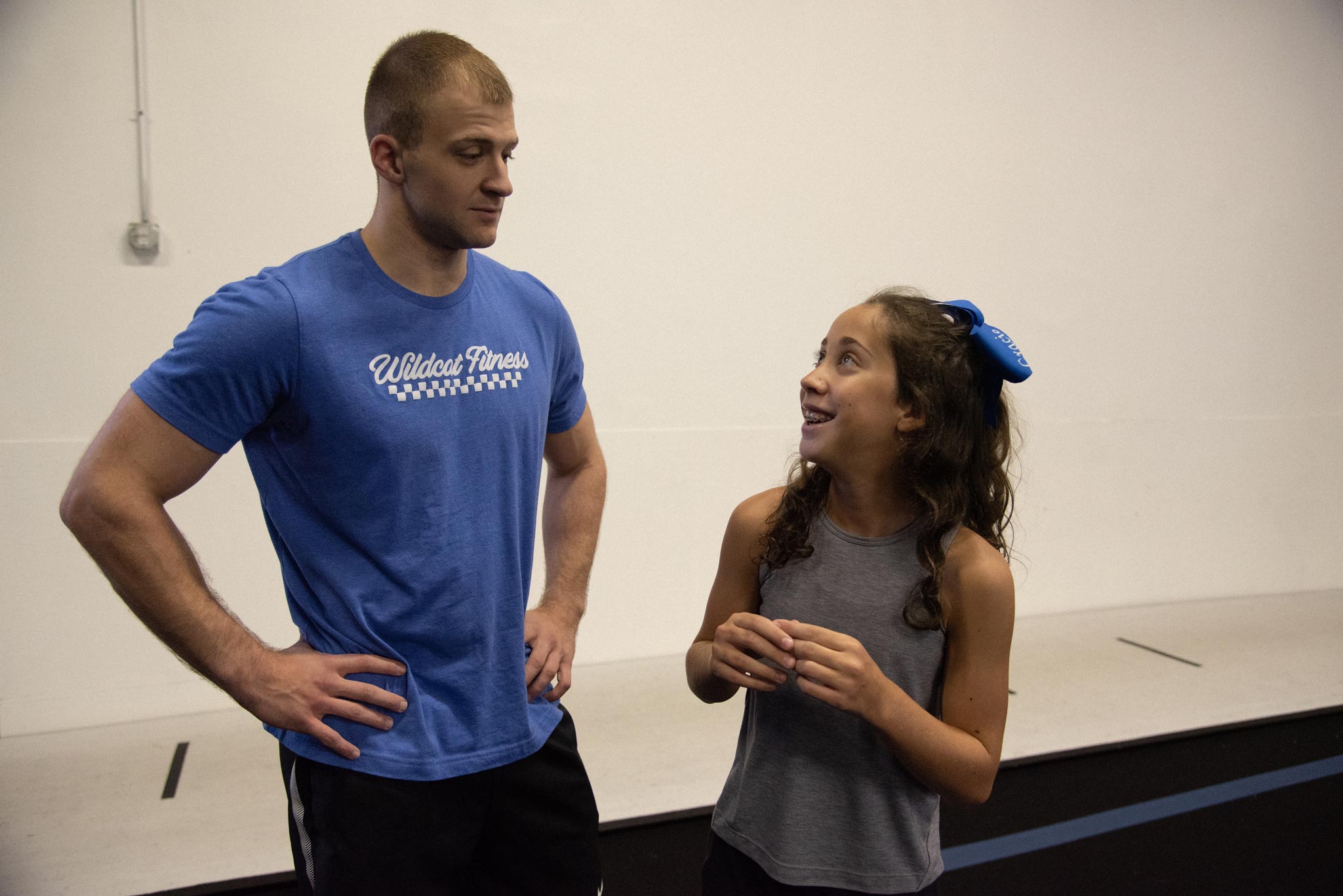Gracie pictured with a young adult male in a gymnasium after practicing cheerleading stunts. She is looking up at him and smiling.