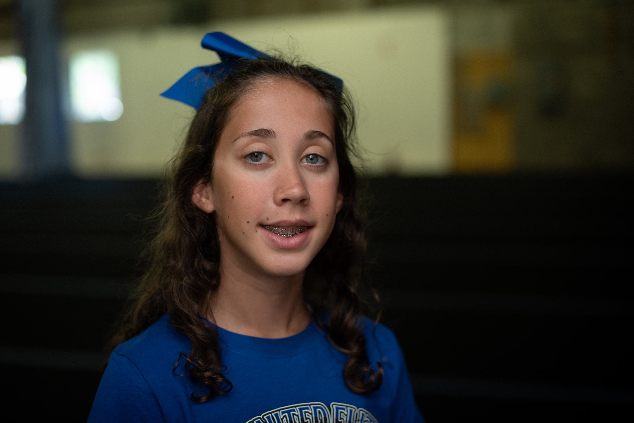 A close-up portrait of Gracie, a high-school-age girl with brown hair. Her hair is loose and curly. She is smiling and has braces.