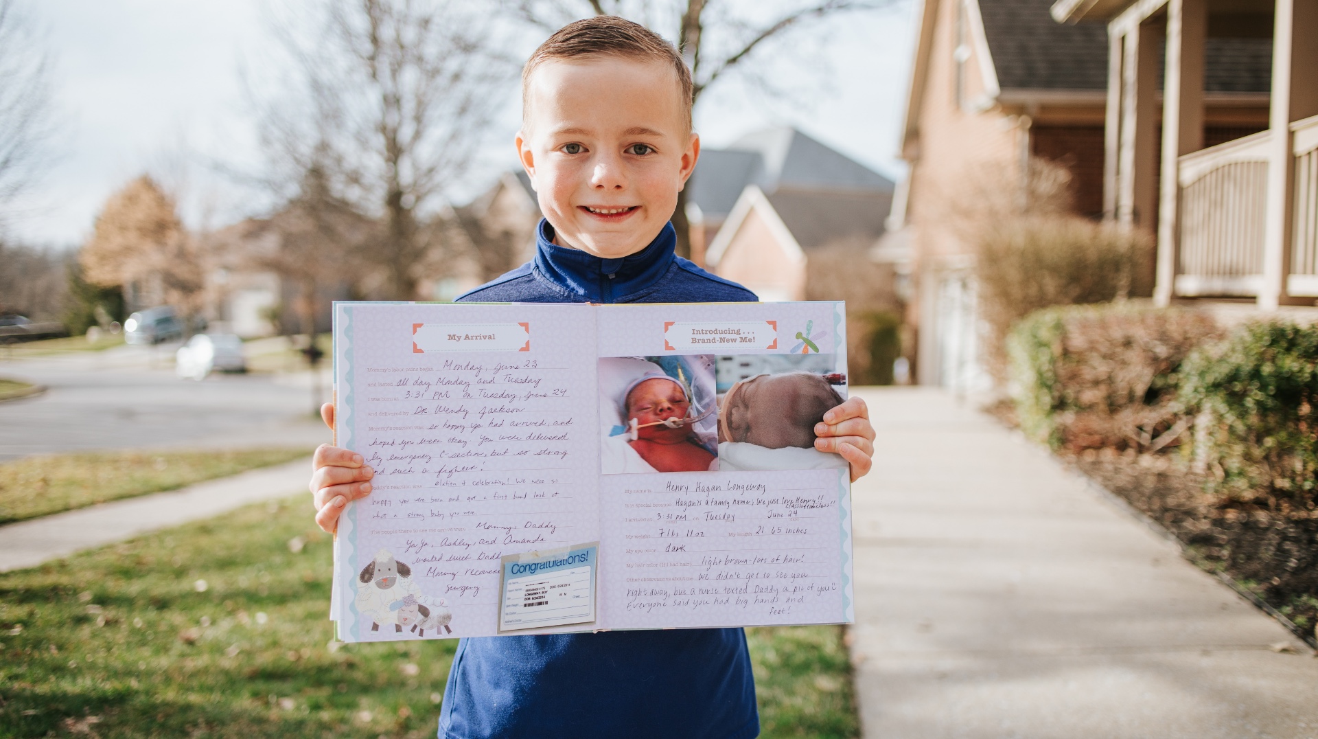 Henry stands outside with a big smile as he holds up a diary with writings and images from his experience as a baby.