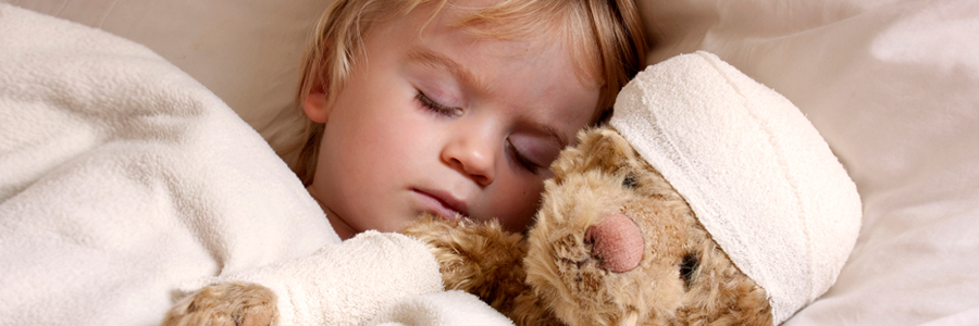 A little boy sleeps in his hospital bed with a teddy bear wearing bandages.