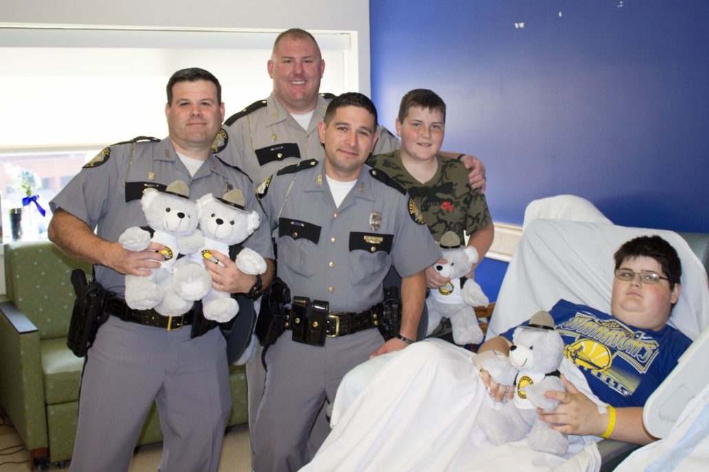 Three Kentucky State Troopers deliver a teddy bear to a boy at KCH with his brother.