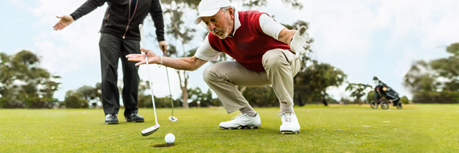 A golfer tries to usher his ball into the hole as his partner watches.