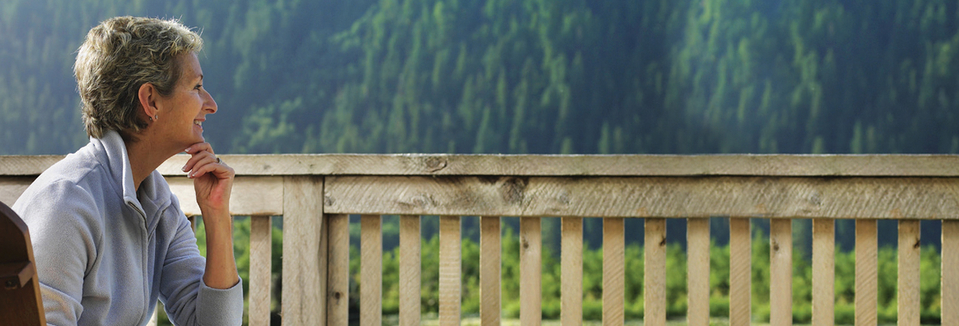 A woman sits on a balcony overlooking hills.