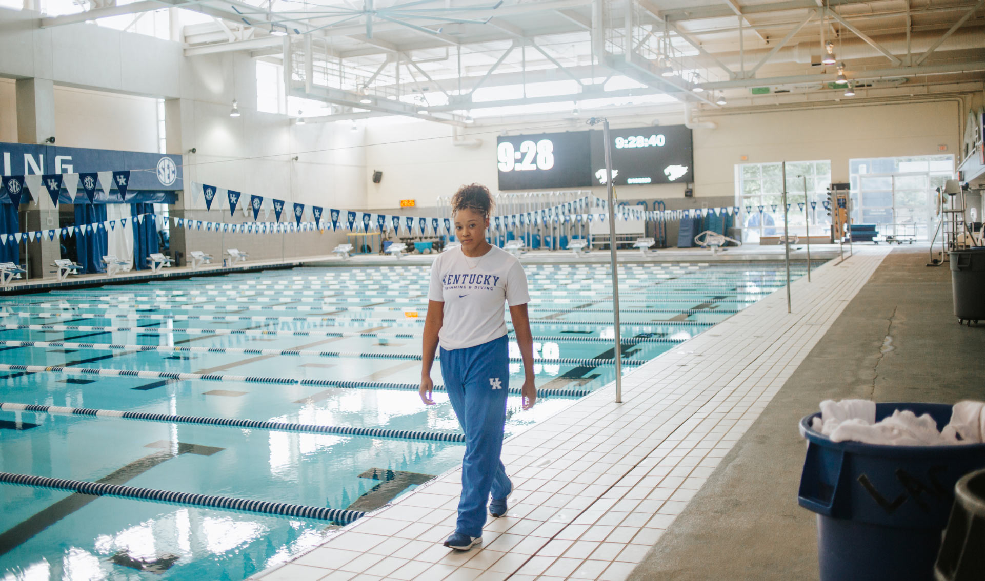 A photo of Jaida, dressed in a white t-shirt and blue track pants, walking alongside the pool.