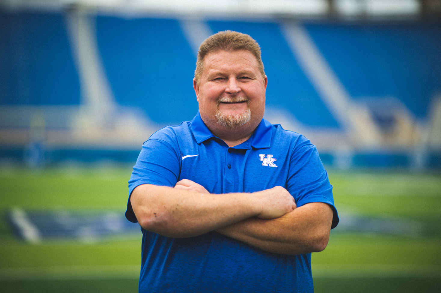 Jimmy crosses his arms and smiles while out on the UK Football field.