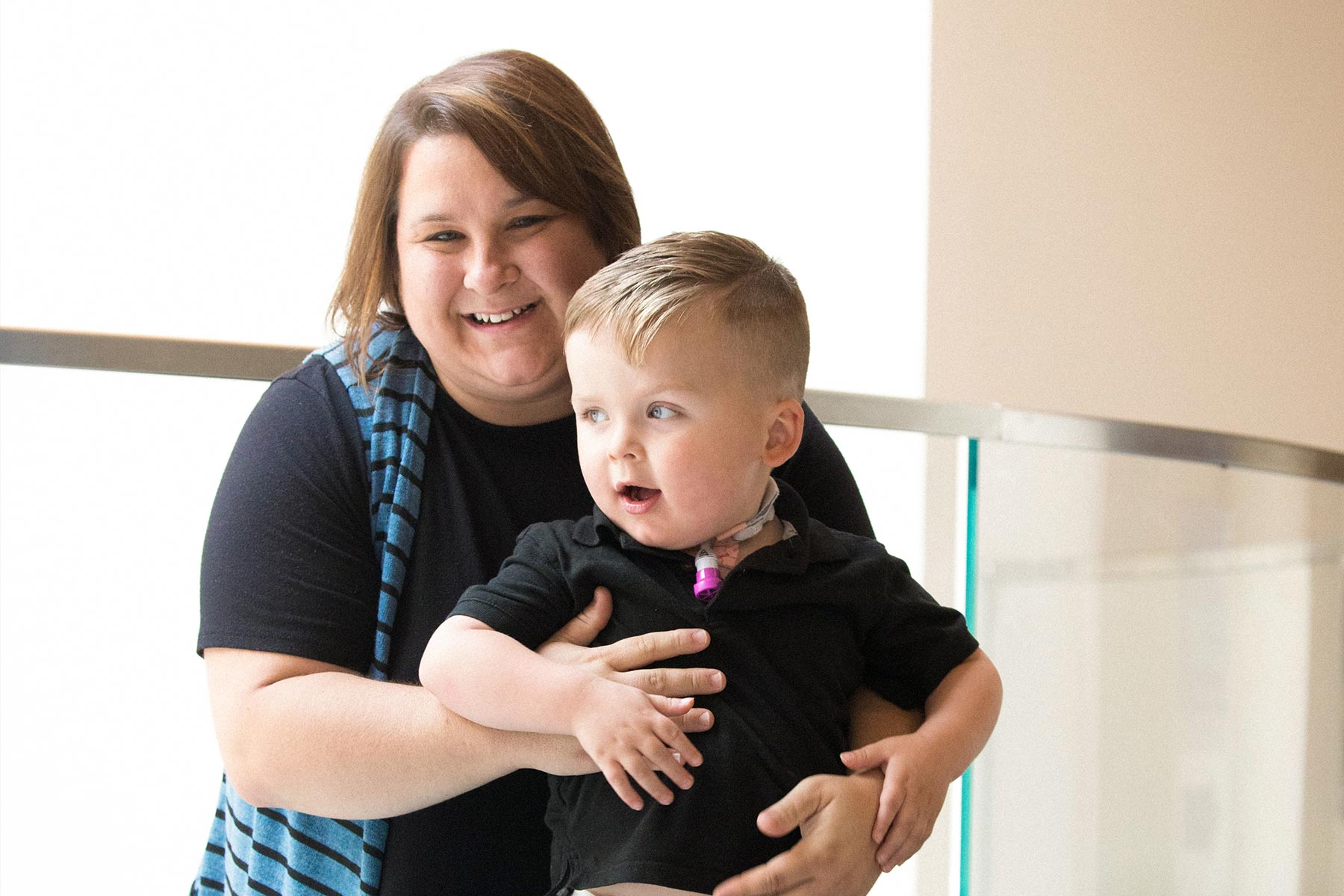 Hannah, Kase's mother, holds a smiling Kase. Kase has a tracheostomy tube in his neck to help him breathe.