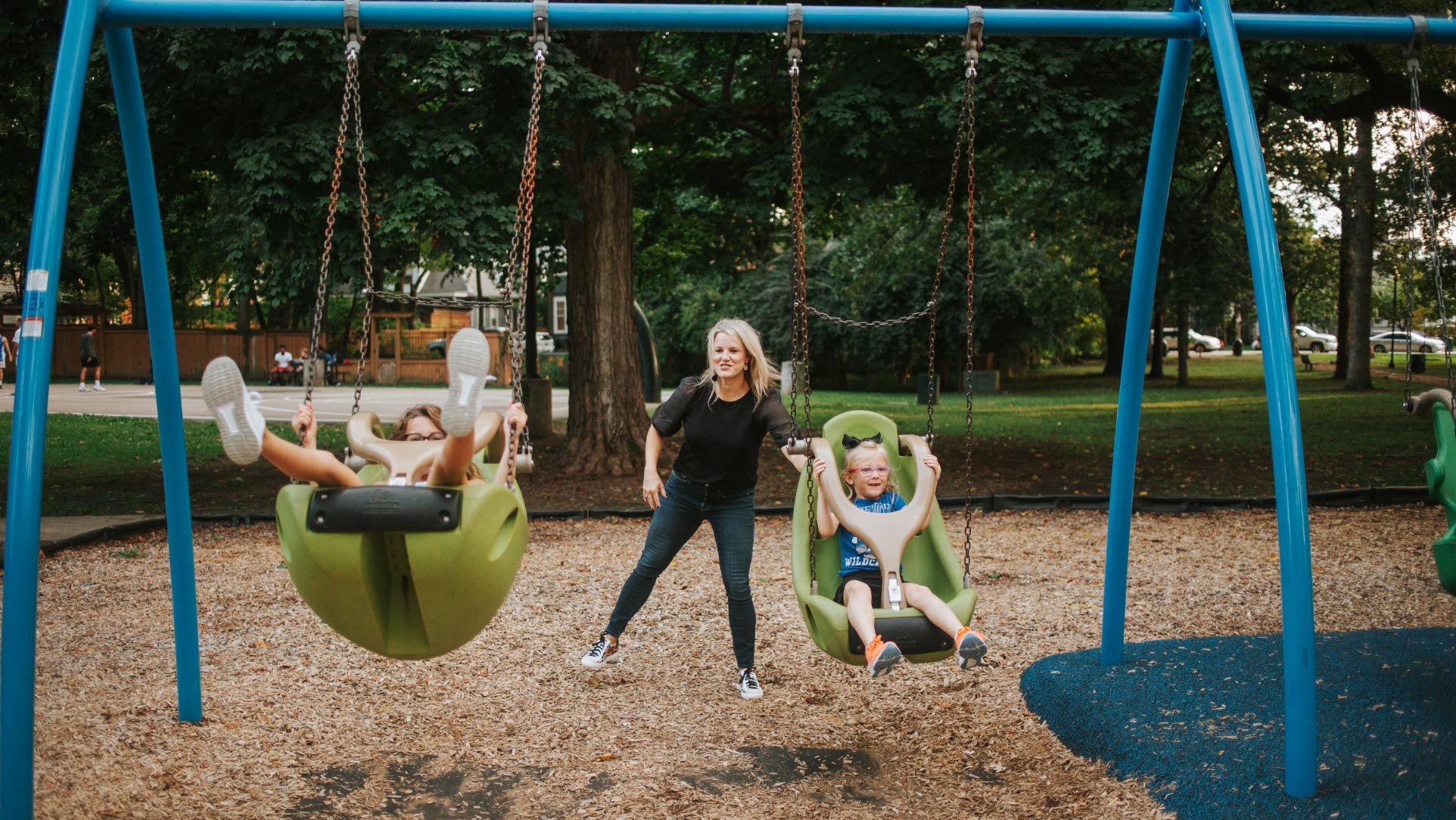 Kelley pushes Gabriella and Olivia on a green swing set at the park.