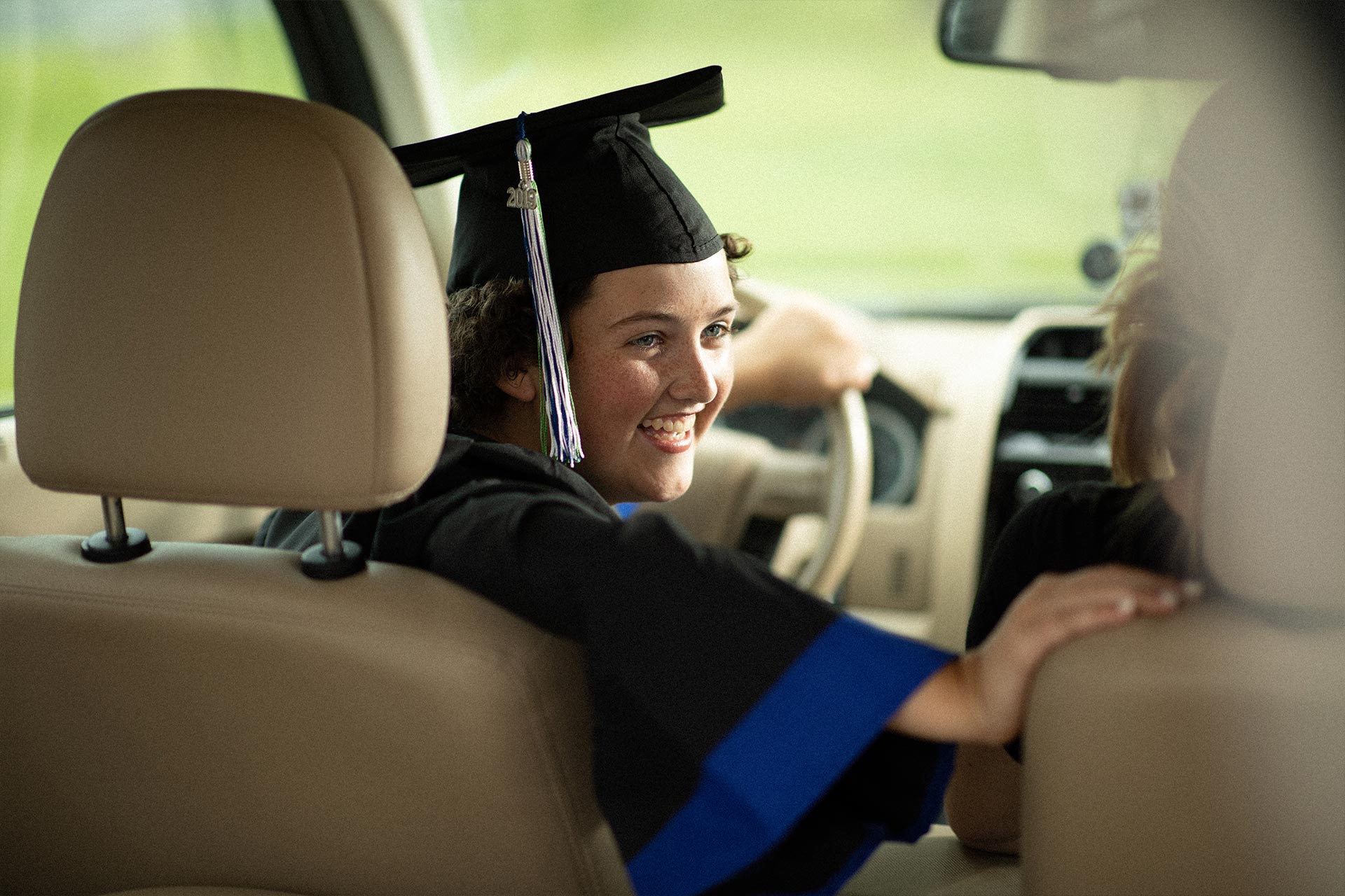 Kylee Tyson sitting in the driver's seat of a car, wearing her graduation cap and gown.