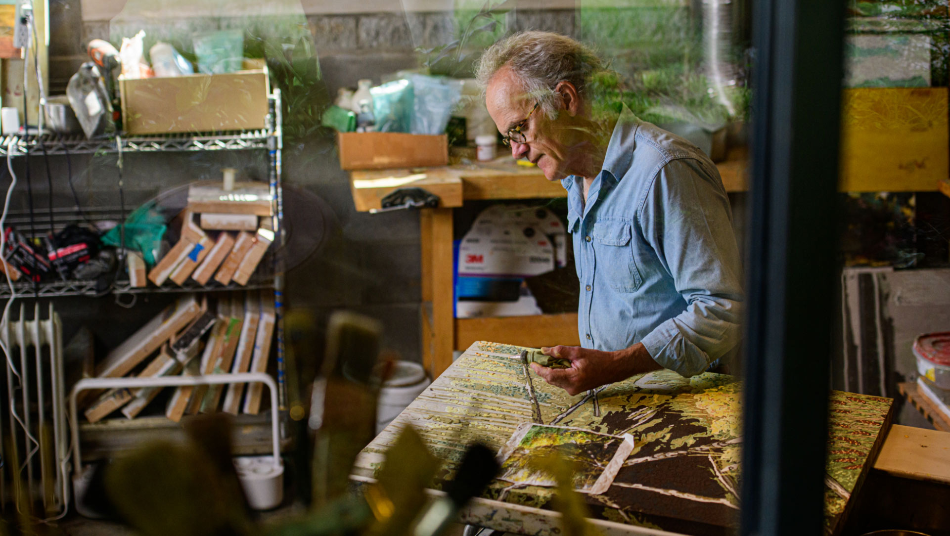 We see Lynn through the window to his studio, working on one of his frescoes.