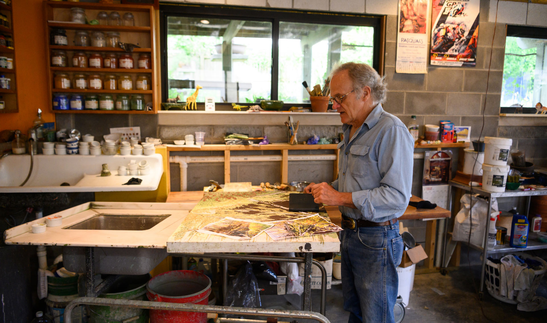 We see Lynn standing at a worktable in his studio in front of an in-progress painting. The painting has several reference photos on it.