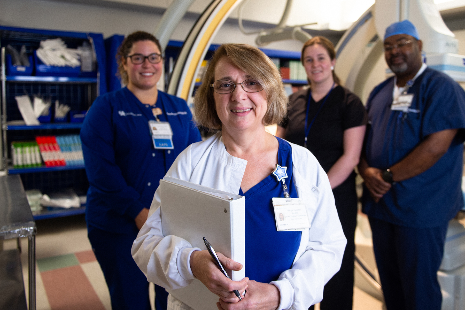 Margie Campbell holds a binder and smiles for a photo with other nurses at UK Healthcare.