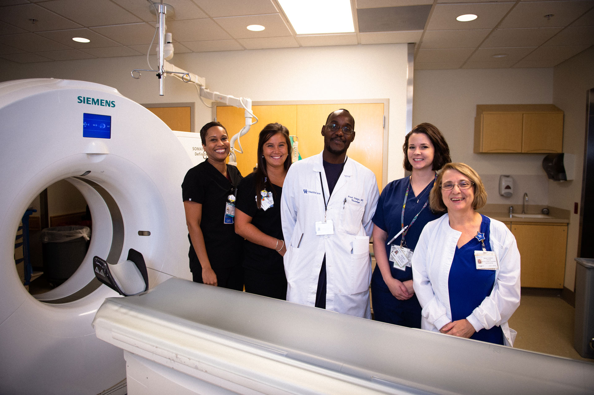 Margie stands and smiles for a photo with a group of nurses next to a CT scanning machine.