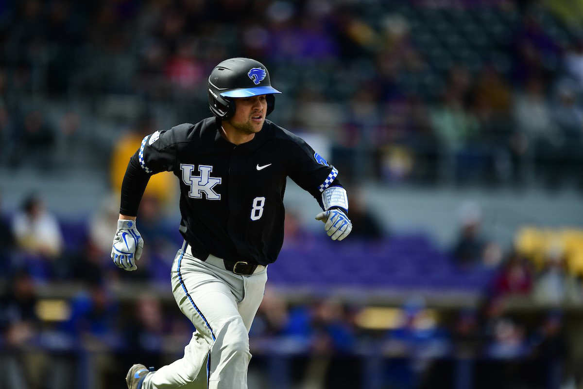 Marshall running across the baseball field in a black and gray UK baseball uniform, including a black helmet and grey gloves.