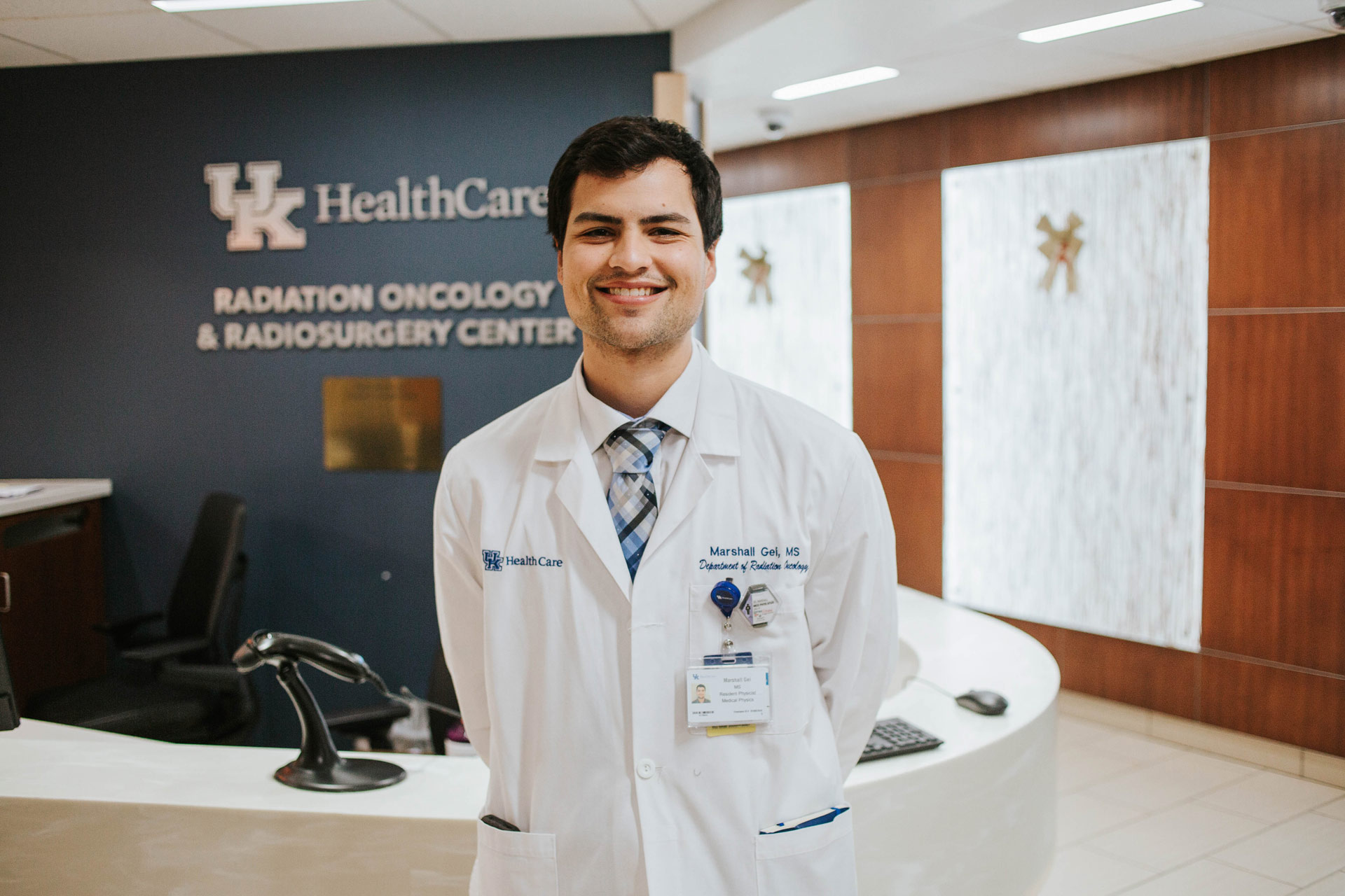 Marshall standing in the UK HealthCare Radiation Oncology and Radiosurgery Center. He is wearing a white doctor’s coat and a blue plaid tie.