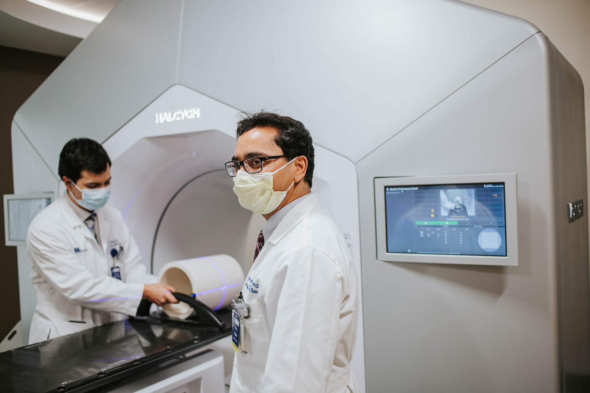 Marshall works on a radiation machine in the background as Dr. Pohkrel turns to the side, showing us his profile.