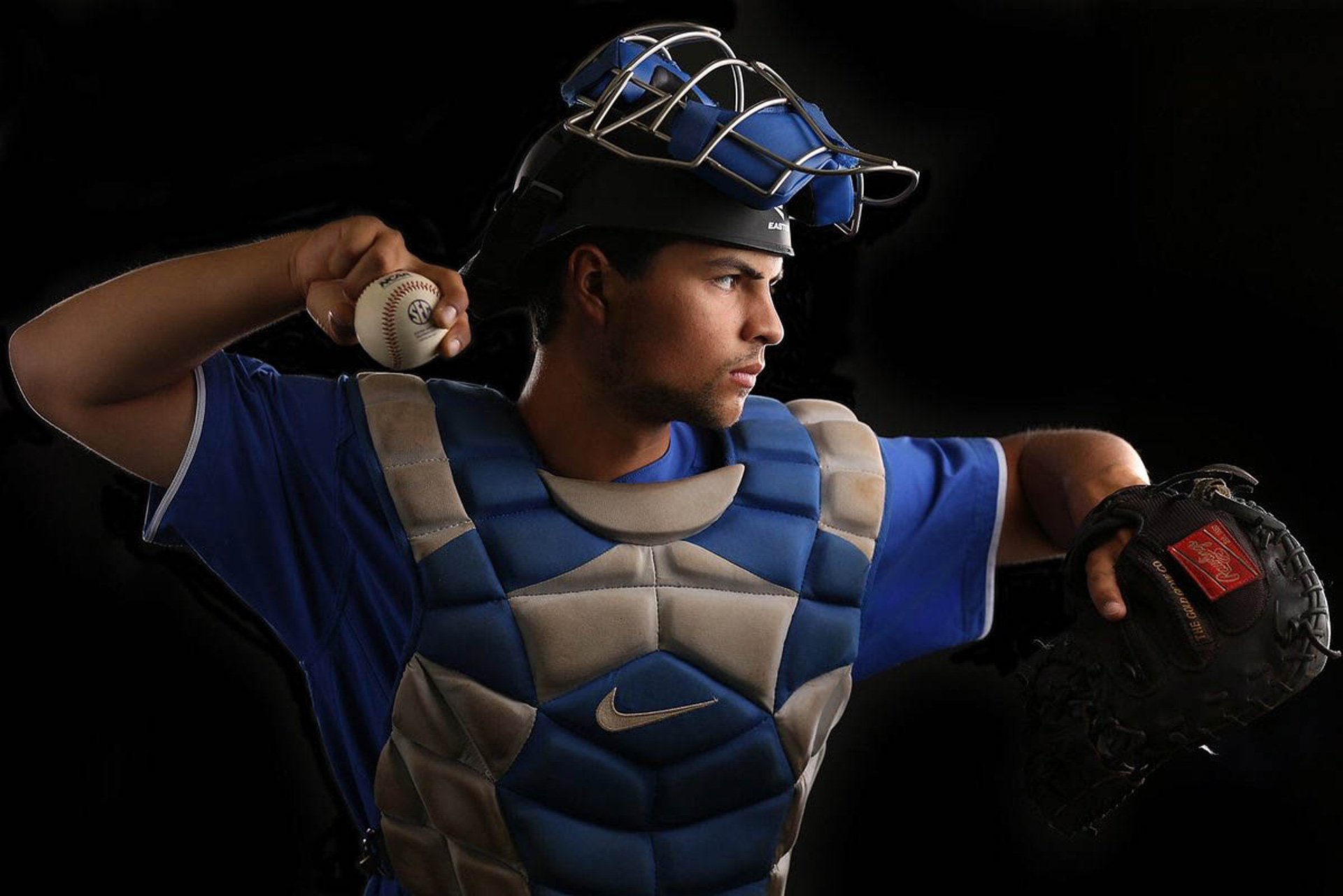 Side profile shot of Marshall Gei, a young adult man with black hair, in his catcher’s gear, with a ball in hand ready to throw.