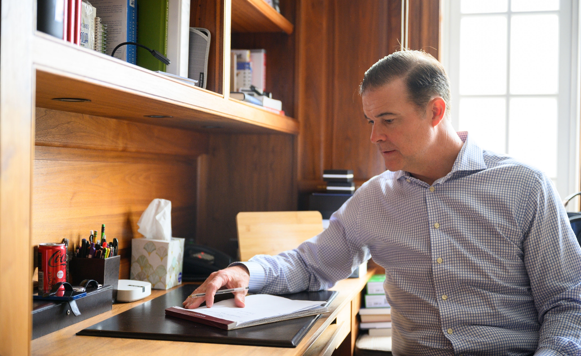 A candid photo of Coach Mitchell at his desk, looking at some papers.