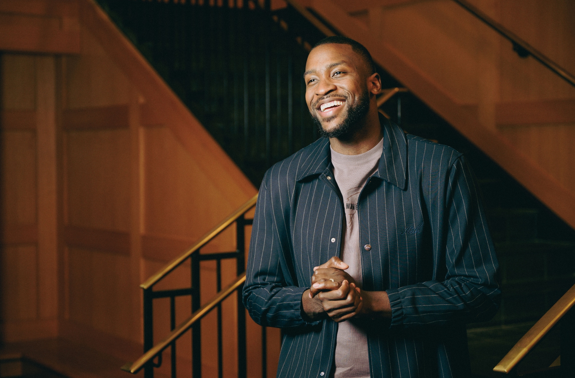A photo of Michael clasping his hands together as he smiles and looks off camera.