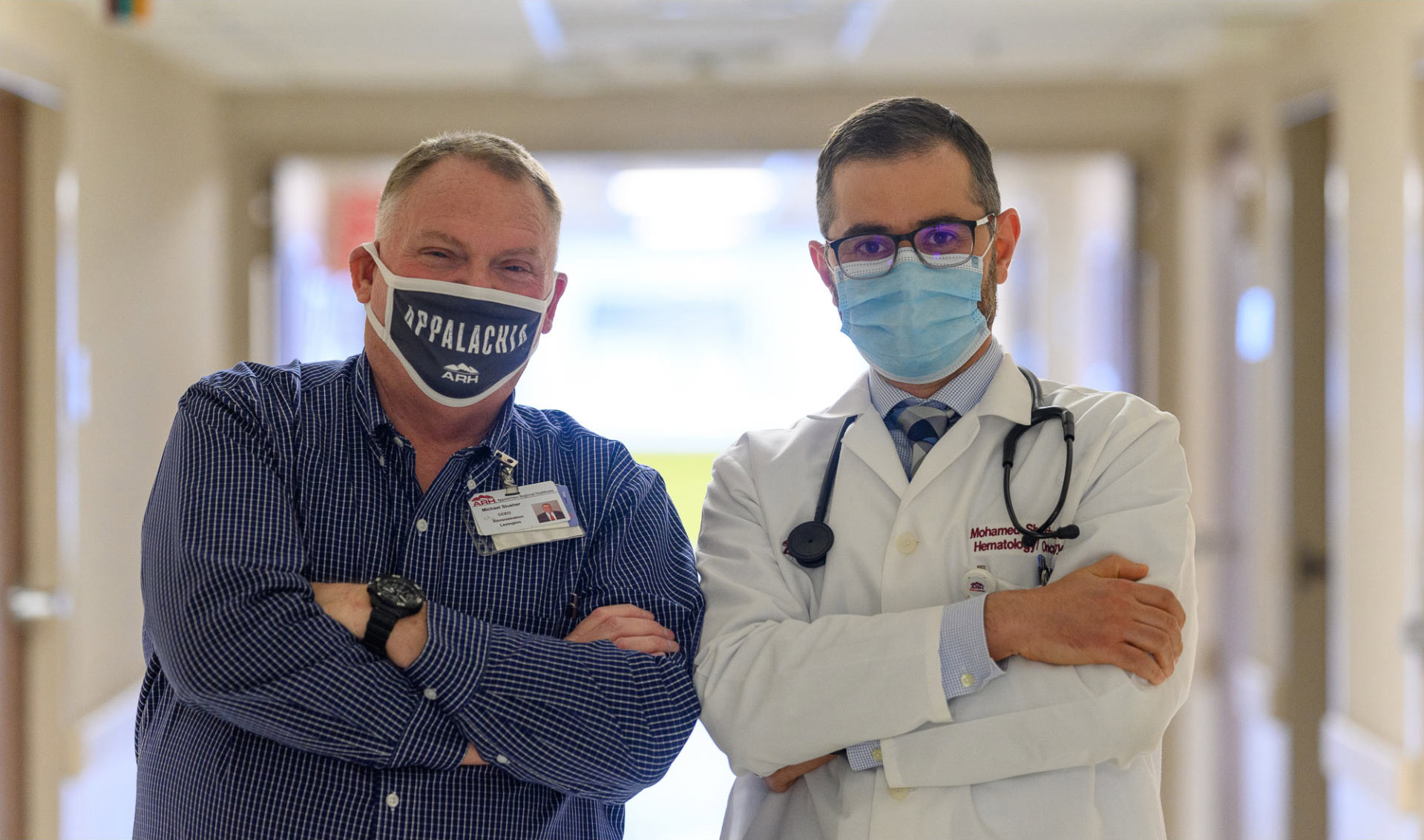A portrait of Michael and Dr. Shanshal, posing with their arms crossed. Both are wearing masks.