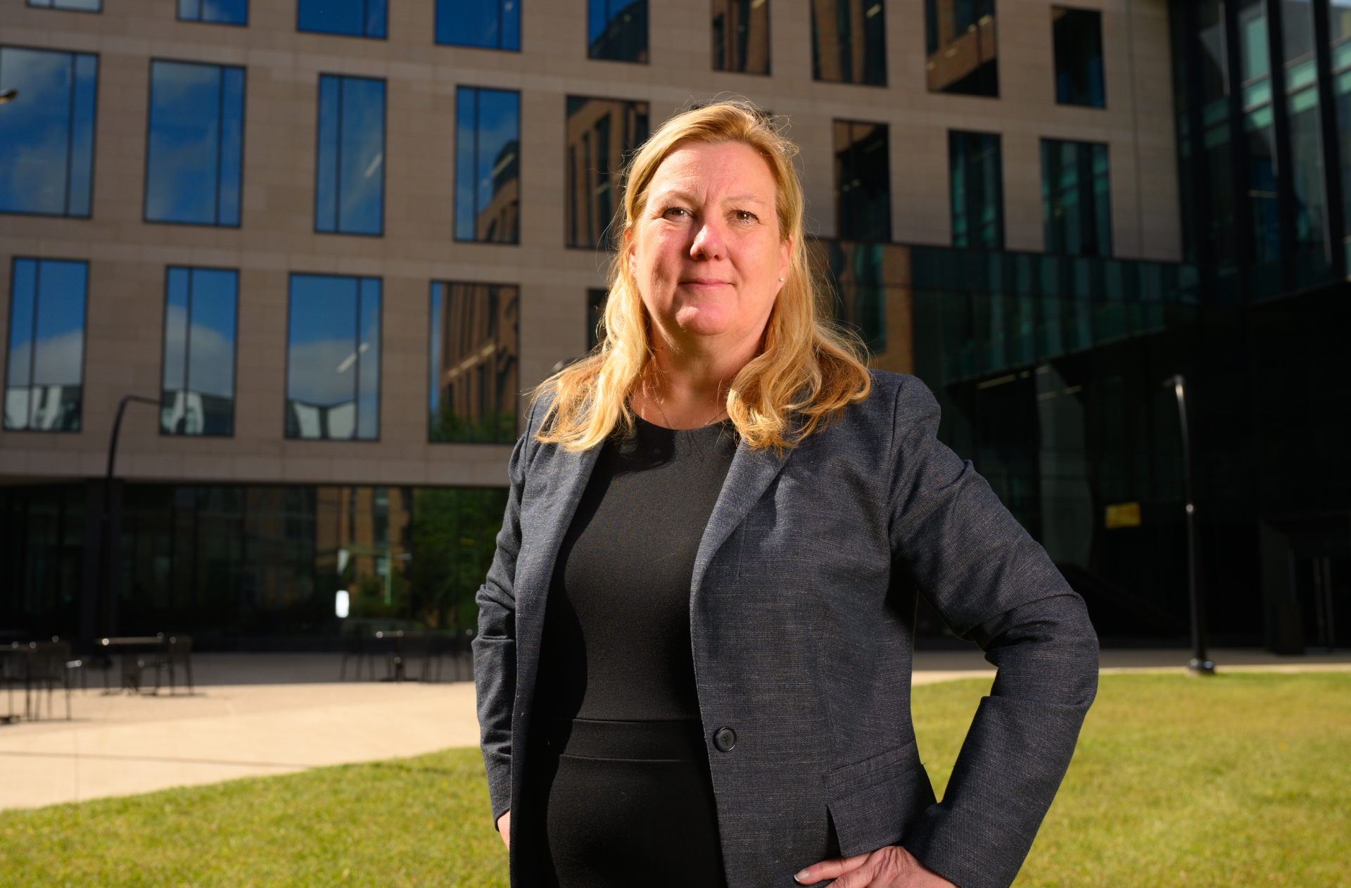 A photo of Dr. Kolesar posing confidently with her hands on her hips in front of a building on the UK HealthCare medical campus.