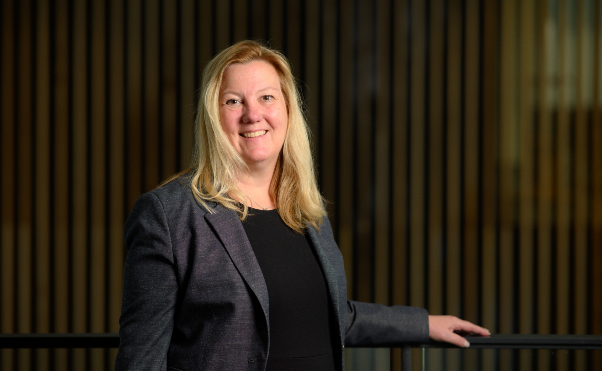 A photo of Dr. Kolesar smiling for the camera as she rests her hand on the back of a chair.
