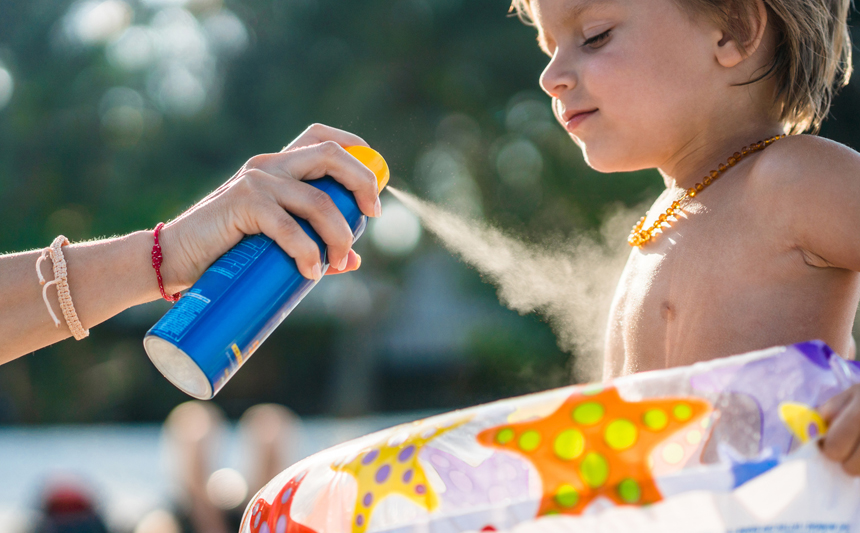 A mother applies sunscreen to her young child at the pool.