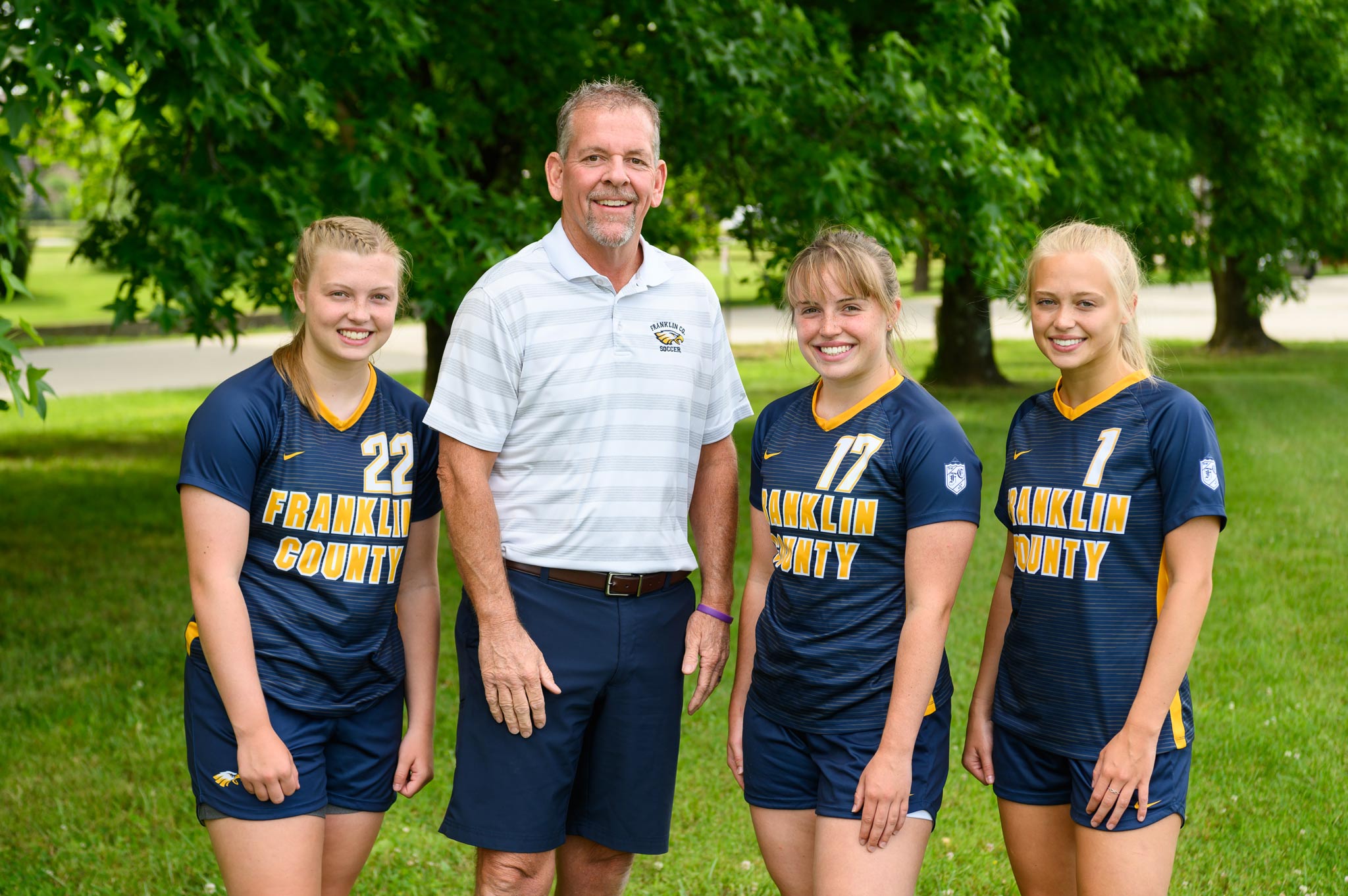 The three girls pose smiling with Coach Jon Sutphin, a tall middle aged man with a beard.